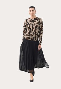 Sweter dzianinowy w panterkę w odcieniach beżu i brązu, połączony z czarną plisowaną spódnicą maxi, z przezroczystego materiału i zwiewnym krojem.