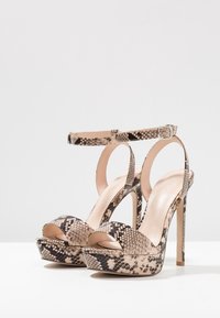 Sandales à talons hauts en imprimé serpent avec une bride à la cheville, bout ouvert et semelle plateforme ; les couleurs incluent beige, noir et marron.