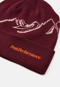 Bordeaux hue hue strikket hue lavet af blødt materiale, med et bjergmønster i lyserød og et orange broderet "Peak Performance" logo.
