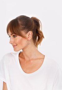 Hoepelringen in roségoud met een gestructureerd ontwerp. Draag van een model met een losse paardenstaart, gecombineerd met een wit T-shirt.