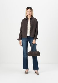 Brown suede jacket with button closure, cream blouse, blue flared jeans, gray heeled shoes, and a small dark handbag.