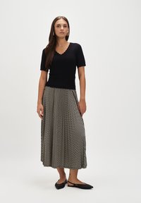 Czarny prążkowany top z falbaniastymi brzegami, w połączeniu z zwiewną spódnicą midi w czarno-białym wzorze oraz czarnymi płaskimi butami.