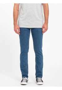 Vaqueros de mezclilla en azul con un corte slim, que presentan un diseño clásico de cinco bolsillos. Combinados con zapatillas de lona en blanco y negro.