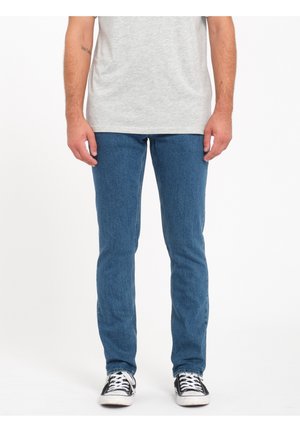 Vaqueros de mezclilla en azul con un corte slim, que presentan un diseño clásico de cinco bolsillos. Combinados con zapatillas de lona en blanco y negro.