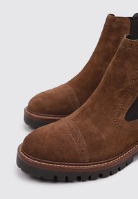 Braune Wildleder-Stiefeletten mit elastischen Seiteneinsätzen, einer runden Spitze und einer strukturierten Gummisohle. Verfügt über Nähdetails und einen niedrigen Absatz.