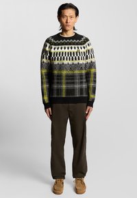 Πλεκτό πουλόβερ σε μαύρο, γκρι και λευκό με κίτρινες πινελιές, με μοτίβα ρόμβων, ρίγες και καρό. Μαύρα ριμπ μανσέτες.