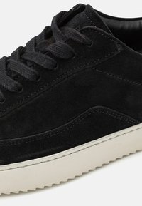 Fekete nubuk sneaker, illeszkedő fűzőkkel, fehér gumitalppal és texturált varrással az oldalán. Alacsony szárú kialakítású.