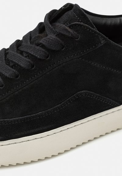 Black suede sneaker with matching laces, a white rubber sole, and textured stitching along the side. Features a low-top design.