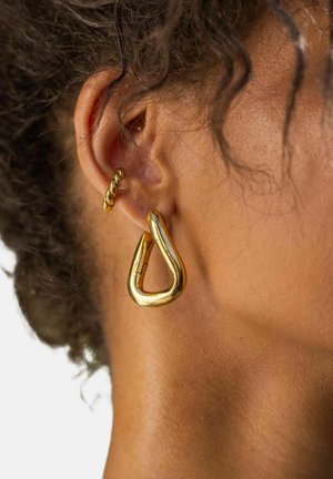 Goldene Creolen mit einem verdrehten Design, die eine glatte, glänzende Oberfläche und eine tränenförmige Form aufweisen, im Ohr getragen.