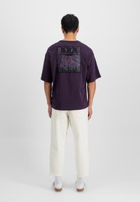 T-shirt en coton violet avec un imprimé graphique représentant une carte de la ville et des silhouettes, associée à un jean droit blanc et des chaussures à enfiler décontractées.