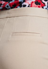 Béžové kalhoty s hladkým povrchem a šikmým žebrováním. Obsahují paspulovou kapsu na zadní straně, minimalistický design a čisté linie.