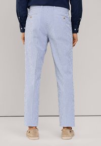 Striped trousers in light blue and white, feature a straight cut, back pockets with buttons, and rolled hems. Textured fabric.