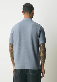 Kortärmad pikétröja i ljusgrått, med ribbat mönster, klassisk krage och sidsprund. Bärs med mörka jeans.