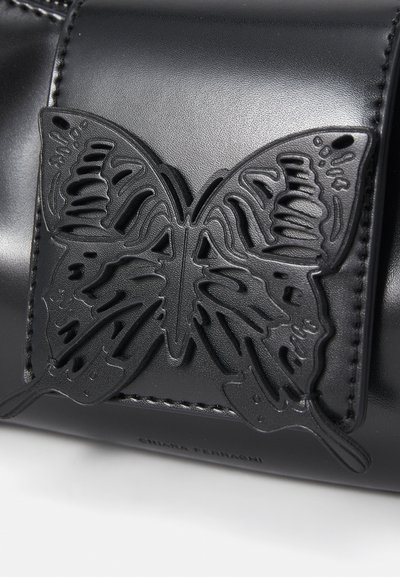 Accessoire en cuir noir avec un design de papillon découpé et détaillé. Une texture notable et des coutures accentuent l'élégance du matériau.