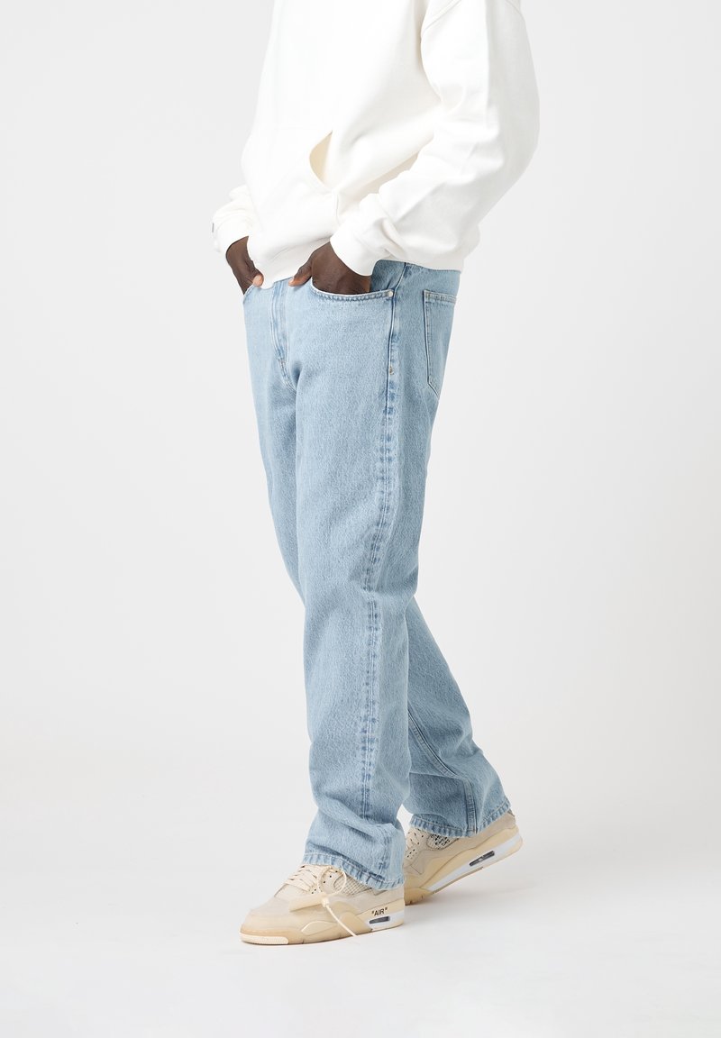 Ljust blå denimjeans med avslappnad passform, med framfickor och en klassisk midja. Bärs med en vit hoodie och beige sneakers.