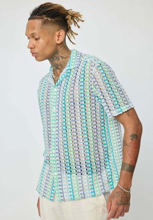 Chemise à manches courtes avec un motif géométrique vert, bleu et blanc. Équipée d'un col, d'une fermeture à boutons et d'une coupe décontractée.