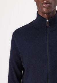 Navy zip-up sweater with a high collar, made of soft knit fabric, featuring a silver zipper and a fitted design. No additional patterns visible.