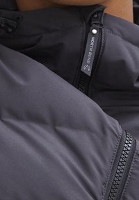 Chaqueta acolchada negra con acabado suave y mate. Cuenta con un bolsillo con cremallera en el lado izquierdo, capucha ajustable y una etiqueta de marca que dice "NORTH BEND".