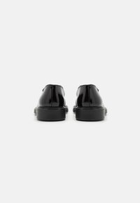 Black patent leather shoes with a smooth finish, featuring a rounded toe and a low, textured black sole, viewed from the back.