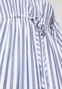 Gestreiftes Hemd mit blauen und weißen vertikalen Linien, mit geraffter Taille und einer Schleifen-Detail, aus leichtem Baumwollstoff gefertigt.