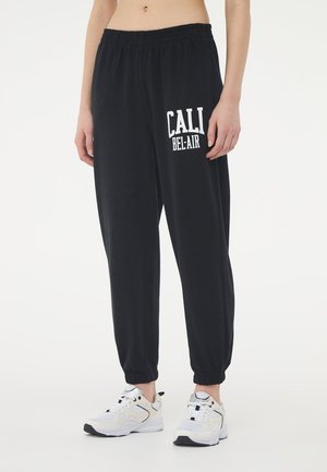 Pantaloni lounge neri con vita elastica e polsini. Testo stampato sul davanti "CALI BEL-AIR" in bianco. Tessuto morbido e leggero. Abbinati a sneakers bianche.
