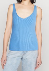 Světle modrý žebrovaný tílko s hlubokým výstřihem do V a širokými ramínky. Hladká pletenina, přiléhavý střih. Kombinováno se světle modrými džíny.