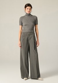 Top grigio a costine con colletto a imbuto e maniche corte abbinato a pantaloni a gamba larga a righe verticali a vita alta. Scarpe beige a punta completano l'outfit.
