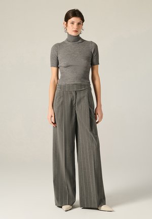 Top grigio a costine con colletto a imbuto e maniche corte abbinato a pantaloni a gamba larga a righe verticali a vita alta. Scarpe beige a punta completano l'outfit.
