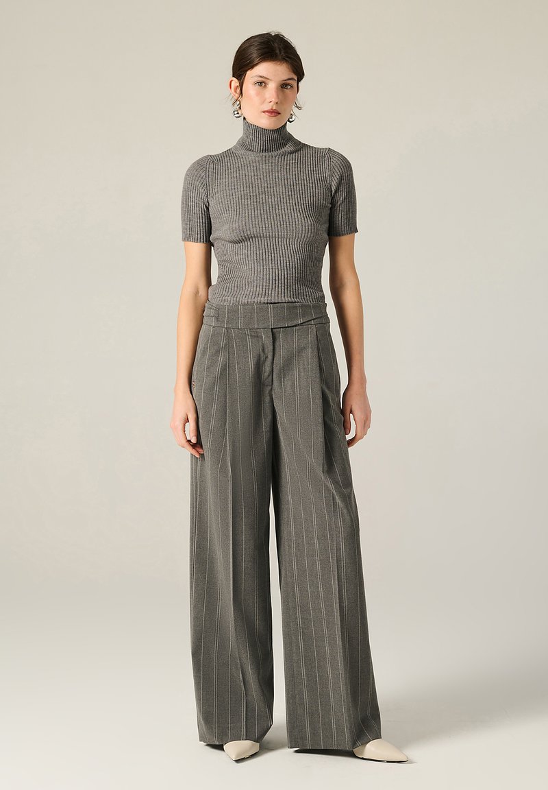 Top grigio a costine con colletto a imbuto e maniche corte abbinato a pantaloni a gamba larga a righe verticali a vita alta. Scarpe beige a punta completano l'outfit.