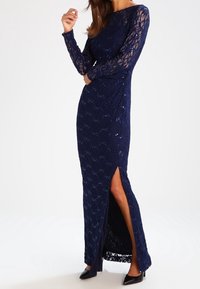 Marinblå spetsaftonklänning med långa ärmar, paljettdetaljer, slits på sidan och en scalloped nederkant. Bärs med svarta högklackade skor.