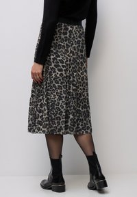 Sukně s plisováním v béžovém a černém leopardím vzoru, vyrobená z měkkého materiálu. Nositelná s černými kotníkovými botami a punčochami, s viditelným přiléhavým páskem.