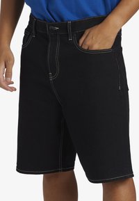Shorts de denim negro con costuras en blanco contrastantes, cierre de cremallera y botón, bolsillos delanteros y traseros, y un diseño de pierna recta.