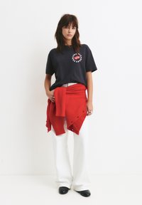 Tricou navy cu un grafic rotund roșu, asortat cu un pulover tricotat roșu legat în talie și pantaloni albi cu picioare largi. Pantofi negri.