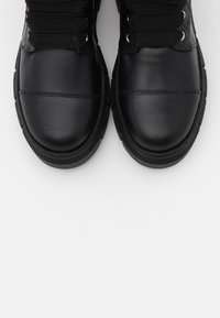 Botas de couro pretas com bicos arredondados grossos, cadarços robustos e solas de borracha chunk nos fundos brancos.