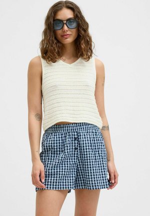 Crème gebreide mouwloze top met een v-hals, gecombineerd met marineblauwe en witte ruitenkorte broek met een elastische tailleband en voorknopjes.