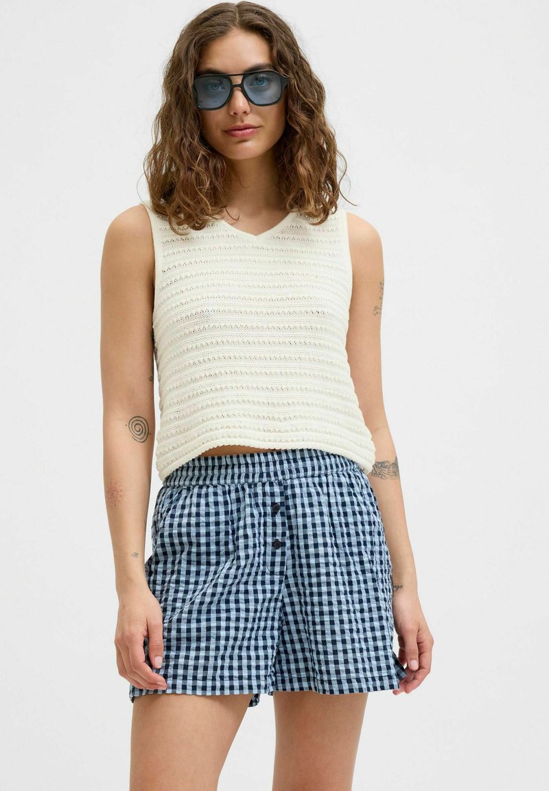 Crème gebreide mouwloze top met een v-hals, gecombineerd met marineblauwe en witte ruitenkorte broek met een elastische tailleband en voorknopjes.