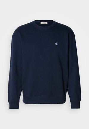 Temno modra majica s kapuco iz mešanice bombaža z rebrastimi manšetami in robom. Ima majhen svetlo moder logotip na prsih. Klasičen kroj okrogle odprtine.