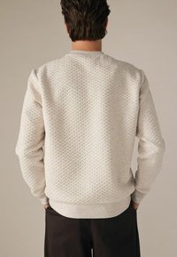 Lys beige sweatshirt med tekstureret zigzag-mønster, ribbede krave og manchetter samt afslappet pasform; tøjet set fra ryggen.