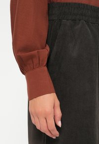 Roestkleurige blouse met lange mouwen en geplooide manchetten, gecombineerd met zwarte korduroy broek met verticale ribbels en een elastische tailleband.