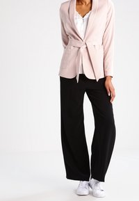 Rosa blazer med knytband i midjan och två framfickor, ihop med svarta vida byxor och vita sneakers. Slät tyg med skräddarsydd passform.