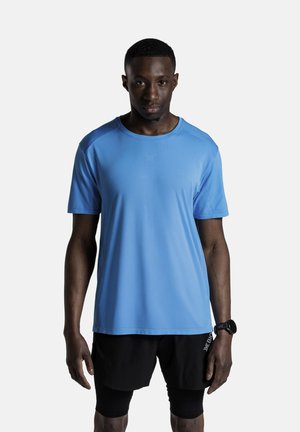 Uomo in piedi, rivolto verso di noi, che indossa una maglietta azzurro chiaro, pantaloncini neri con leggings integrati e un orologio da polso nero.