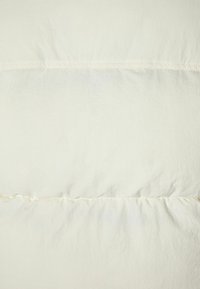 Vit kviltad täcke med en mjuk, slät textur; har horisontell sömnad och en lätt lyster; lätt och plyschig design.