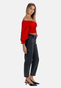 Top corto rojo con los hombros al descubierto, con smocking texturizado y mangas largas abullonadas, combinado con unos vaqueros negros de cintura alta y unos tacones negros tipo slingback.