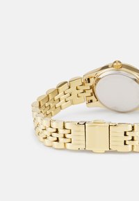 Gold-Uhrenarmband aus Edelstahl mit einem Mesh-Armband, rundem Ziffernblatt und einer Krone an der Seite. Die Rückseite ist glatt und unmarkiert.