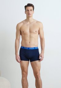 Dunkelblaue Boxershorts aus elastischem Stoff mit einem blauen Logo-Bund. Einfaches Design, körpernahe Passform, glatte Textur.