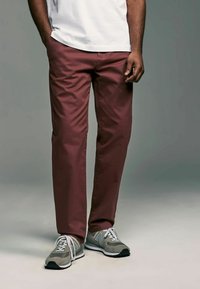 Chinos bordeaux en tissu mélange de coton, avec une coupe ajustée et des poches latérales. Associés à des baskets grises New Balance.