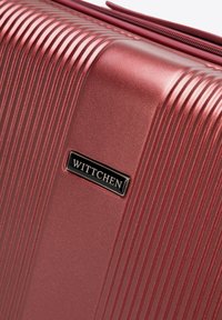 Wittchen Hartschalenkoffer in Metallic-Rot mit vertikaler Rillenstruktur, glatter Oberfläche und einem schwarzen Logo-Highlight auf der Vorderseite.