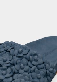 Μπλε σανδάλι με υφή στην επιφάνεια και διακοσμητικές ανθισμένες λεπτομέρειες. Το λουράκι είναι στολισμένο με ανάγλυφα, στρωματοποιημένα σχήματα λουλουδιών.