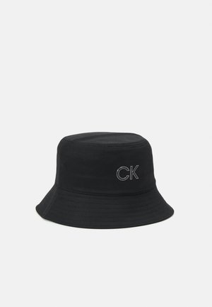 Zwarte bucket hat met gestikte brede rand en wit "CK"-logo op de voorkant in het midden tegen een effen witte achtergrond.
