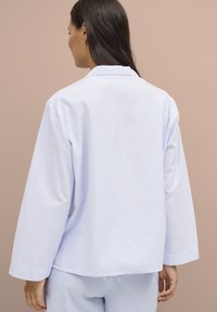 Camicia a maniche lunghe a righe blue chiaro e bianche con colletto. Presenta una vestibilità comoda e una texture morbida. La vista posteriore non mostra ulteriori dettagli.